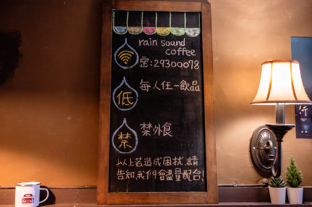 雨聲咖啡店內的手寫黑板公告,寫著 WiFi 名稱 rain sound coffee、低消每人任一飲品、禁外食