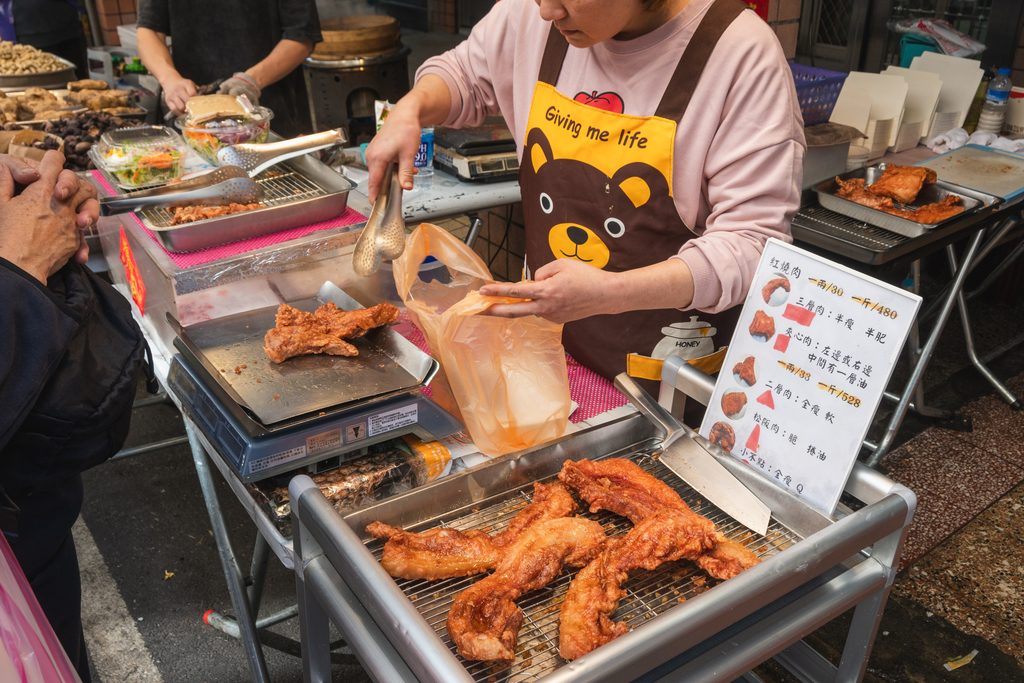 阿角紅燒肉採秤重計費，攤位上擺著電子磅秤與價目卡，老闆娘正在裝袋