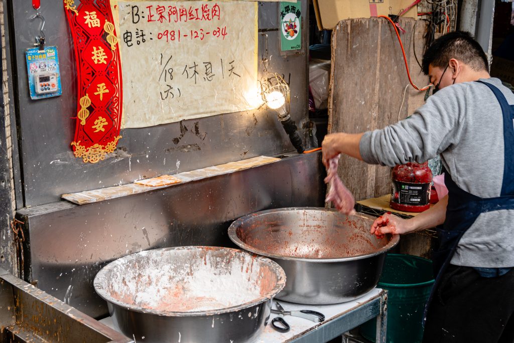 阿角紅燒肉店員手拿一條醃好的豬肉，準備放進紅色醬料盆再抹上一層醬