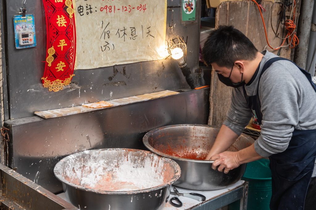 阿角紅燒肉攤位上的兩個大鐵盆，前面是白色裹粉盆、後面是紅色醬料盆，店員正在盆裡拌肉