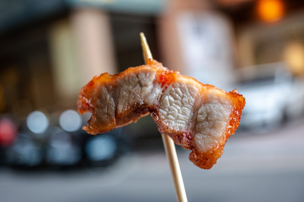 竹籤舉起一片阿角紅燒肉的三層肉，看得到瘦肉、肥肉與炸得酥脆的外殼三層結構