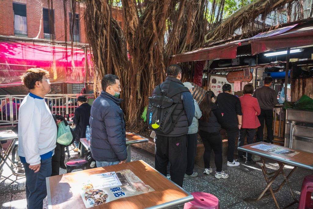 慈聖宮美食街阿桂姨攤位前的排隊人潮，前方是空著的用餐桌