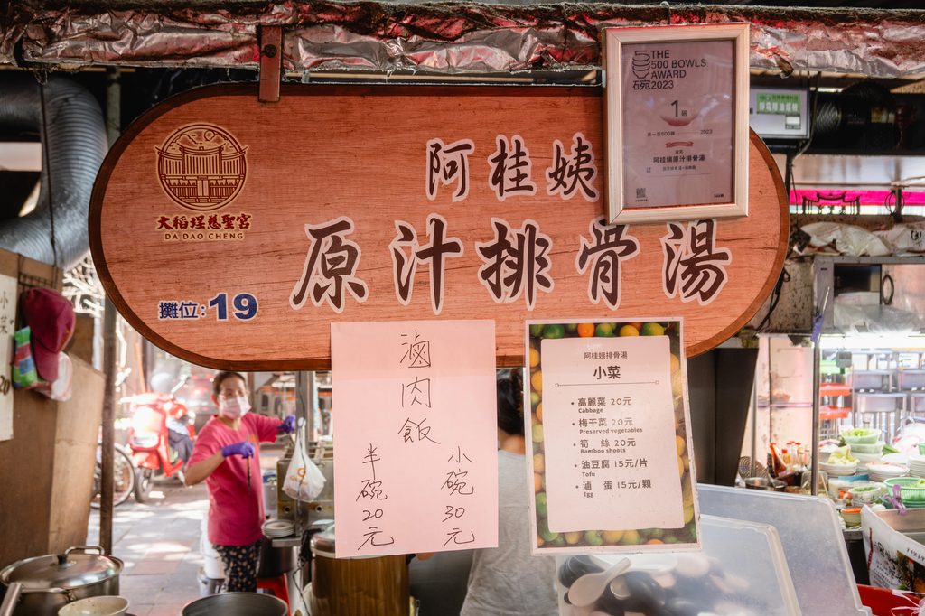 阿桂姨原汁排骨湯攤位招牌，寫著大稻埕慈聖宮、攤位19，旁邊掛著 THE 500 BOWLS AWARD 2023 第1屆的獎項證明，下方是小菜價目牌