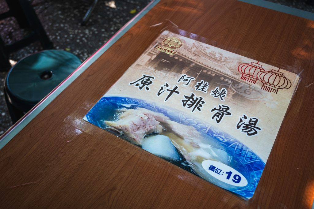 慈聖宮廟埕桌面上的店家標示牌，印著阿桂姨原汁排骨湯與攤位19