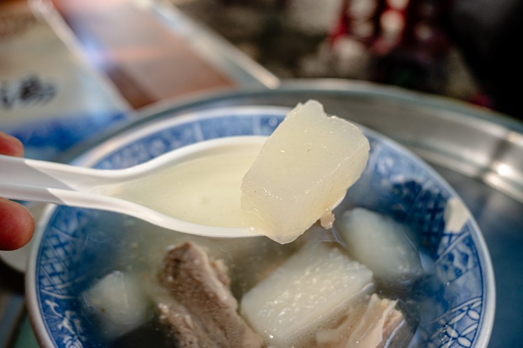 湯匙舀起一塊燉到半透明的白蘿蔔，背景是排骨湯