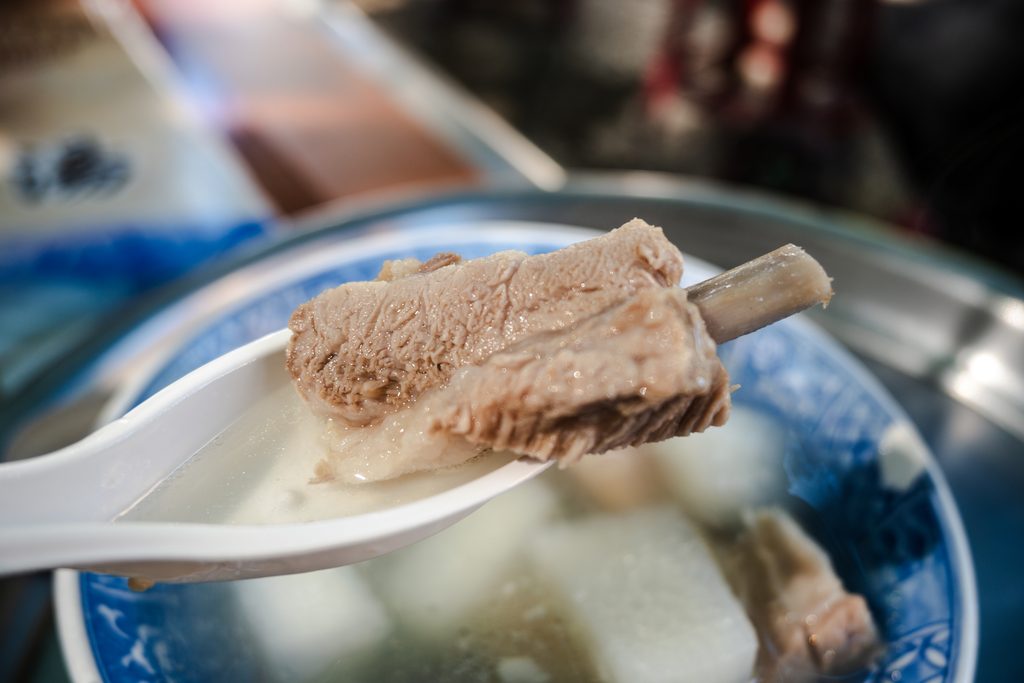 湯匙舀起一塊排骨特寫，肉質軟嫩，可見軟骨