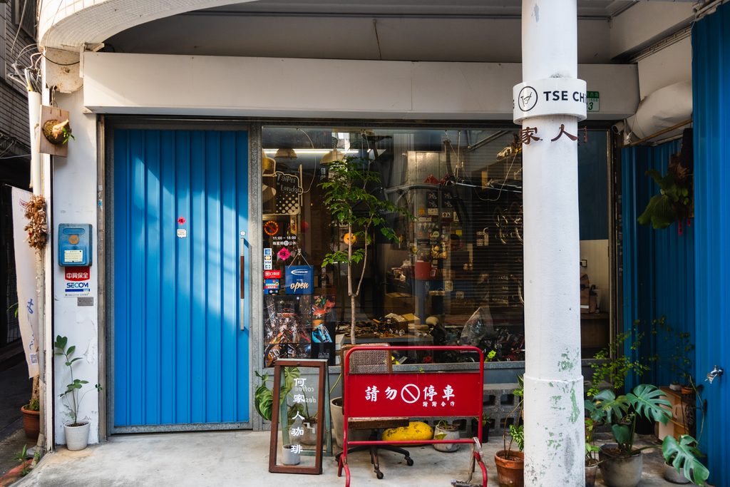 何家人珈琲一樓入口,藍色鐵門的自行車店門面,門口立著木框招牌與盆栽