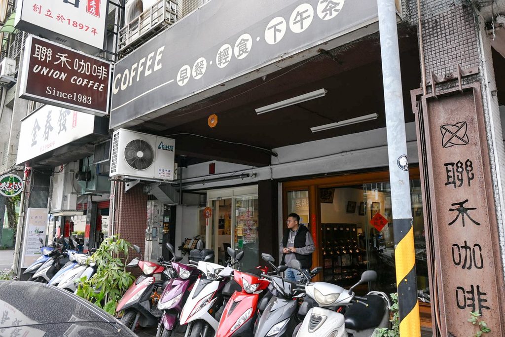 騎樓下的聯禾咖啡招牌,上頭寫著 UNION COFFEE 與 Since 1983,旁邊直式木牌寫著聯禾咖啡,門前停著一排機車