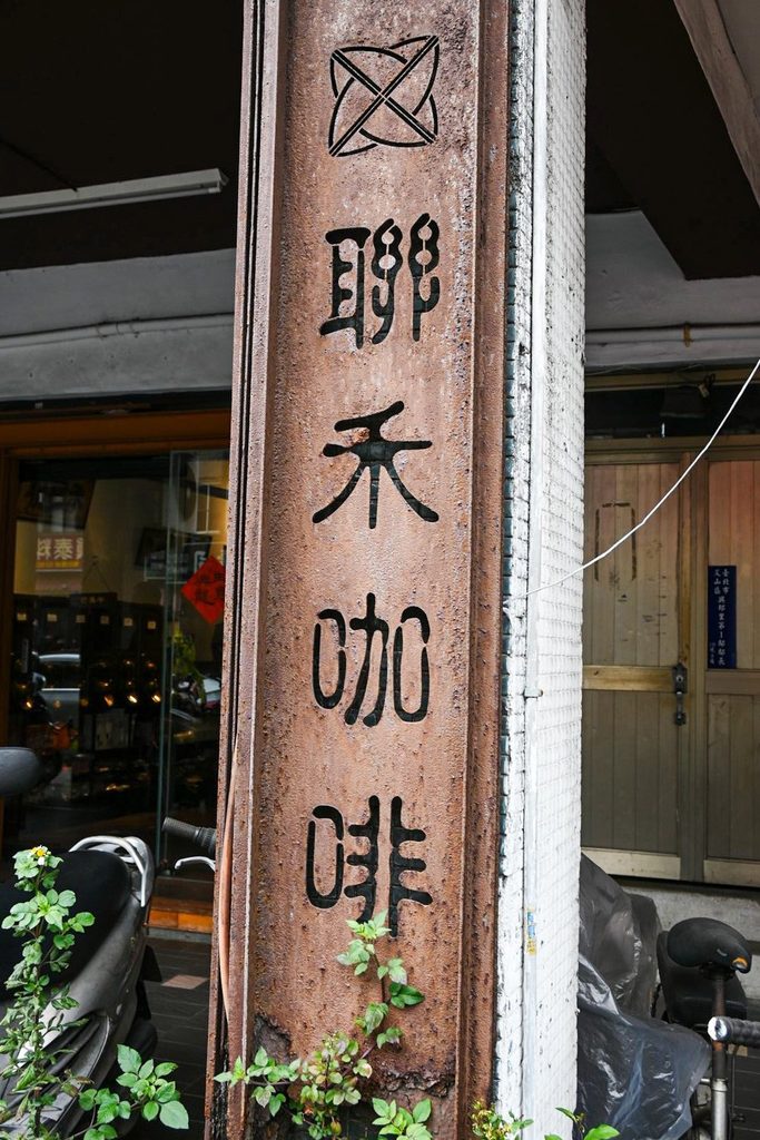 騎樓上方一塊深色木匾,用篆體刻著聯禾咖啡四個字,匾額上方垂著綠色植栽