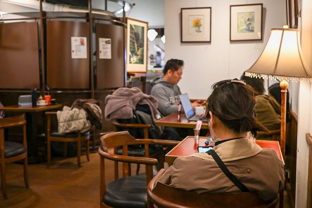 店內後半段,光線較暗,牆上掛著裱框畫作,桌邊立著一盞米色燈罩的立燈,客人各自在座位上